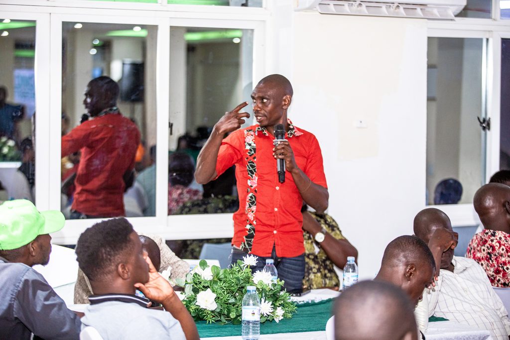 A participant in a red shirt speaks into a microphone among seated attendees at Hima Cement’s customer engagement in Lira.
